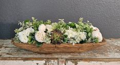 an arrangement of white flowers and greenery in a wooden bowl