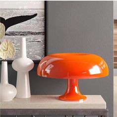 an orange lamp sitting on top of a table next to two white vases and a painting