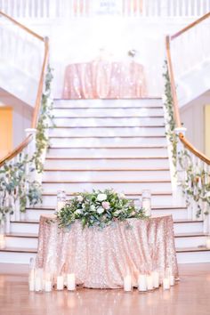 a table with candles and flowers on it in front of a staircase decorated with greenery