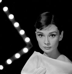 a black and white photo of a woman with gloves on her shoulder, looking at the camera