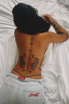 a woman laying in bed with her back turned to the camera and tattoos on her body
