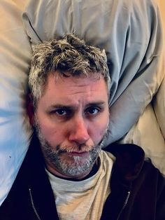 a man laying in bed with his head on the pillow and looking at the camera