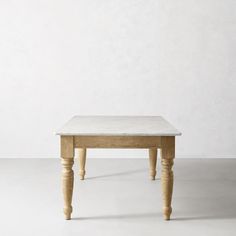 a white table sitting on top of a floor next to a gray wall and wooden legs