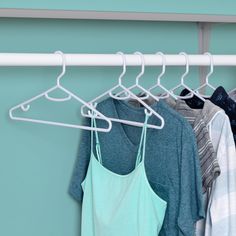 several shirts hanging on a rack in front of a blue wall and a green wall