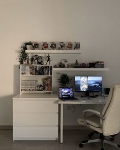 a white desk with two computers on top of it and shelves filled with pictures above