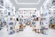 two women in white dresses are walking through a book store filled with shelves full of books