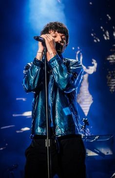 a male in a blue jacket and black pants holding a microphone to his ear while standing on stage