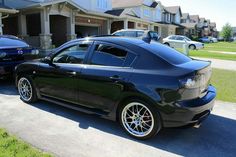 a black car parked on the side of a road next to another car in front of some houses