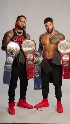 two men standing next to each other holding wrestling belts