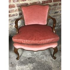 an old fashioned chair with red velvet upholstered on the back and arms, in front of a brick wall