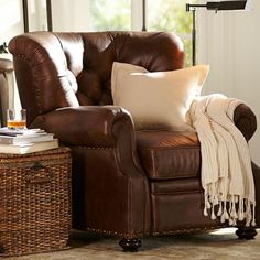 a brown leather chair with pillows and a blanket on top of it next to a wicker basket