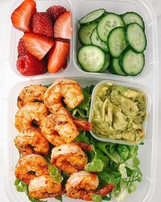 a plastic container filled with salad and shrimp next to cucumber, strawberries