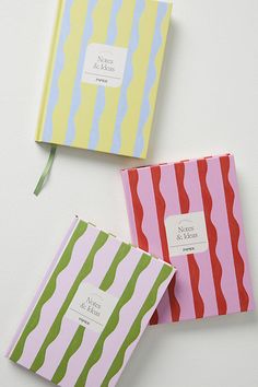 three different colored notebooks sitting next to each other on top of a white surface