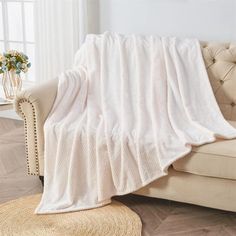 a couch with a white blanket on top of it next to a rug and window