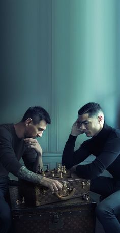 two men sitting next to each other with chess pieces in their hands on top of an old trunk