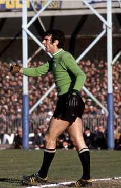 a man standing on top of a soccer field holding a ball in his hand and wearing black shorts