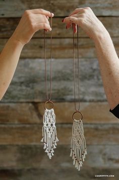 two hands are holding small white macramellas on copper chains, one is dangling from the other