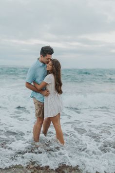 a man and woman standing in the ocean with their arms around each other as they kiss