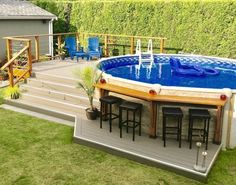 an above ground swimming pool surrounded by grass and wooden decking with bar stools