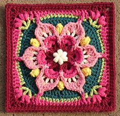 a crocheted square with a flower on the center in pink, green and yellow