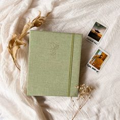 an open book sitting on top of a bed next to some pictures and dried plants