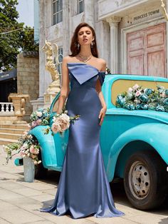 a woman standing in front of an old blue truck with flowers on the bed and wearing a dress