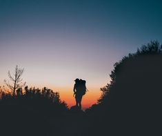 the silhouette of two people with backpacks at sunset