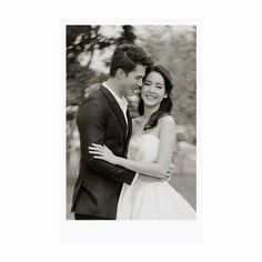 a black and white photo of a bride and groom hugging each other in front of a tree