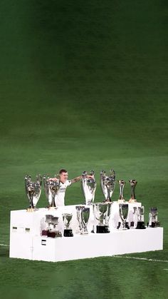 a man standing on top of a white box with lots of trophies in front of him