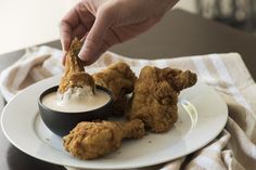 a person dipping something into a small bowl on a plate with chicken wings and ranch dip