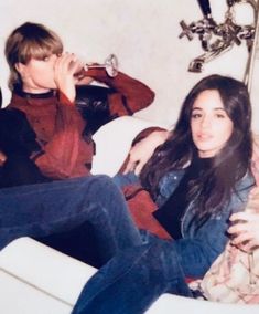 two people sitting on a couch drinking from wine glasses and looking at the camera,