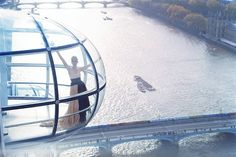 a woman standing on top of a glass structure next to a river with boats in it