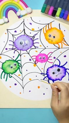 a child's hand is drawing on a spider web with colored crayons