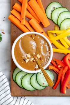 a wooden cutting board topped with cucumbers, carrots, and peanut butter