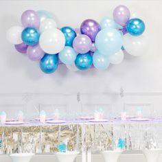 a table topped with lots of balloons next to white wine glasses and dessert tables covered in frosting