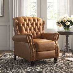 a brown leather chair sitting on top of a rug next to a table with flowers