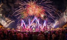 fireworks are lit up in the night sky over a crowd at an outdoor event with palm trees