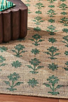 a wooden table sitting on top of a rug covered in green and white flowers next to a chess board