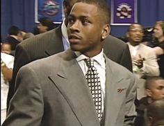 a man in a suit and tie walking through a room with other people behind him