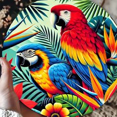 a person holding up a colorful plate with two parrots and tropical leaves on it