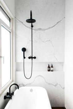a white bath tub sitting under a window next to a wall mounted faucet