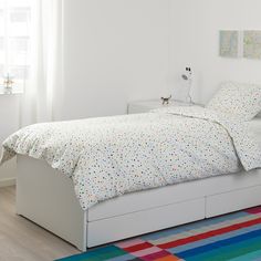 a white bed sitting on top of a wooden floor next to a colorful area rug