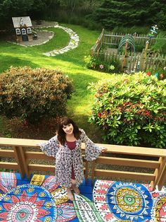 a woman standing on top of a wooden deck next to a lush green yard and garden