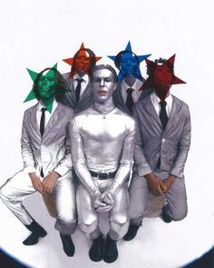 four men in white suits with red, green and blue stars on their heads