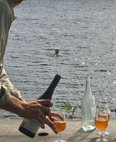 two glasses of wine are being poured in front of a man on the water's edge