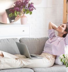 a woman sitting on a couch with her laptop in front of her, looking up at the sky