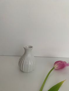 two tulips sitting next to a small white vase on a table with one pink flower in the foreground