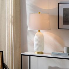 a white lamp sitting on top of a table next to a framed picture and a window