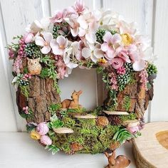 a wreath made out of logs with flowers and deer figurines on it next to a log