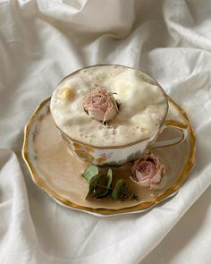 a tea cup and saucer with pink roses on it sitting on a white cloth